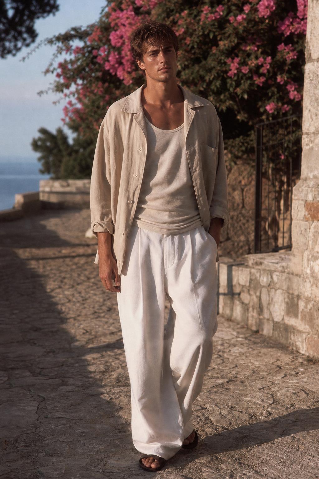 Mediterranean resort menswear — sand linen camp-collar shirt and flowing ivory linen trousers on a villa path